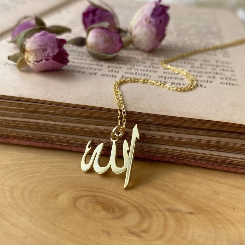 Gold Allah pendant necklace lying on an open vintage book next to dried rosebuds.
