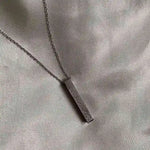 "Silver rectangular engraved pendant necklace on a soft satin fabric background."