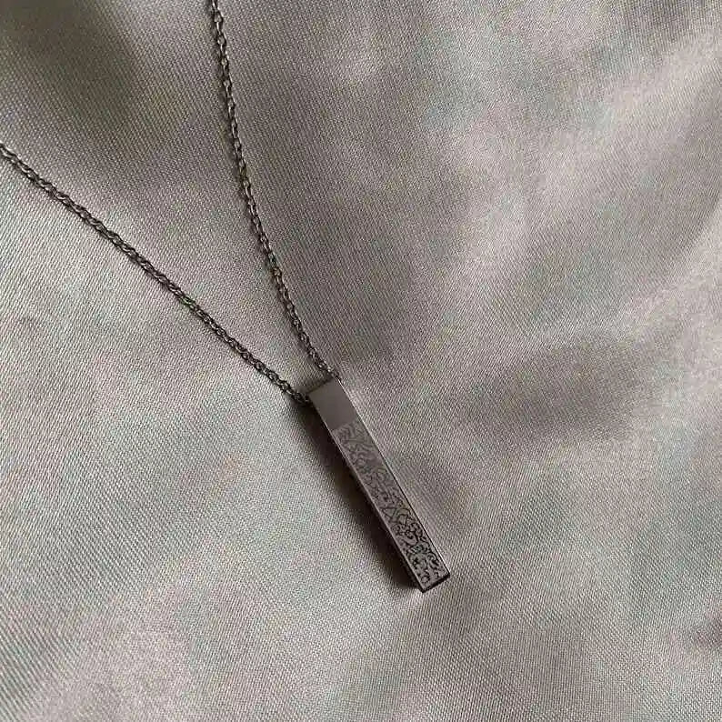 "Silver rectangular engraved pendant necklace on a soft satin fabric background."