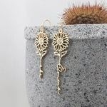 Birth flower custom name drop earrings featuring floral detailing and personalised script lettering in a long elegant design, shown in golden finish.