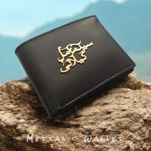 Personalized black leather wallet with customized gold Arabic script name emblem displayed on a stone surface.