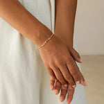 Close-up of a hand wearing a gold bracelet with 'ALEXANDRA' on a neutral background