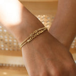 Gold bracelet with engraved names on a wrist against a blurred background