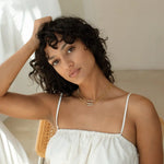 Woman with curly dark hair wearing layered gold chains with custom block name pendants