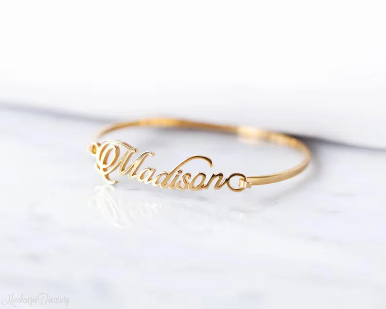 Custom name bangle featuring a script-style personalised name across a sleek open cuff bracelet design.