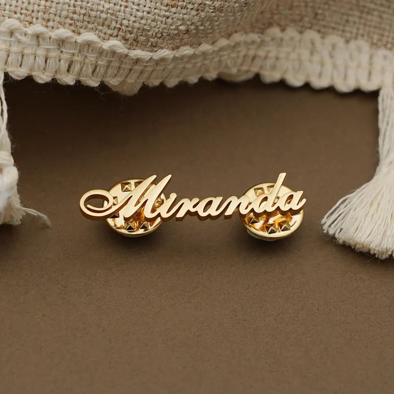 Custom name statement brooch featuring elegant script lettering over a detailed circular backdrop, displayed in a golden finish.