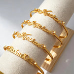 Custom script name cuff bracelets displayed on a jewellery stand, featuring flowing personalised lettering on polished open cuff designs