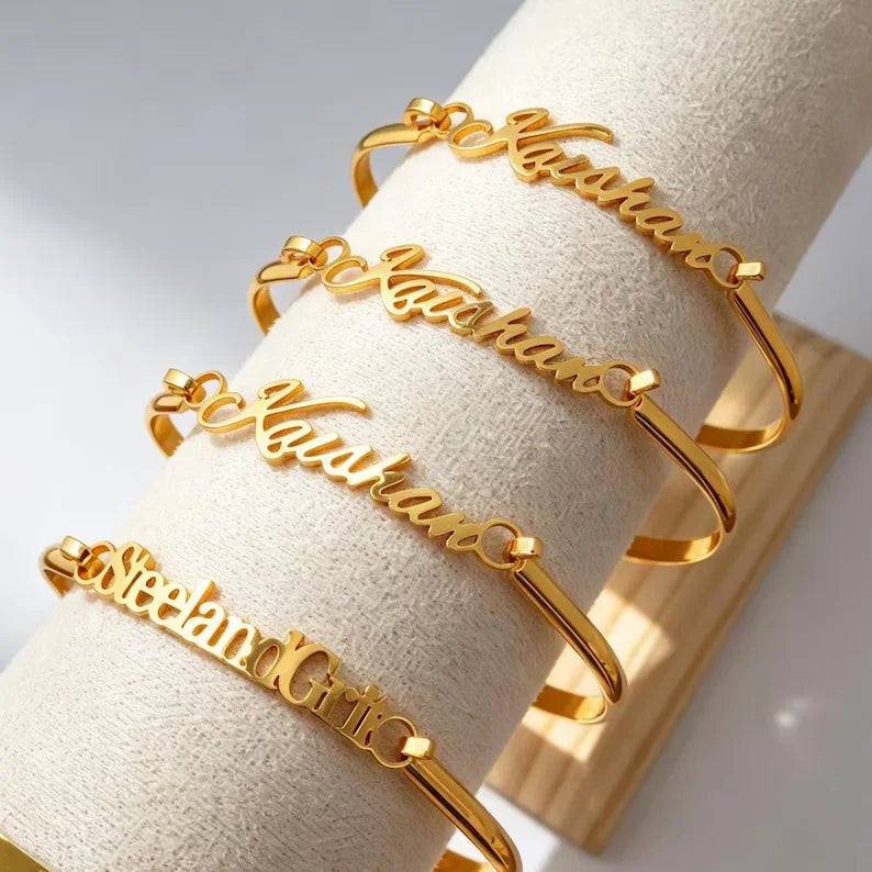 Custom script name cuff bracelets displayed on a jewellery stand, featuring flowing personalised lettering on polished open cuff designs