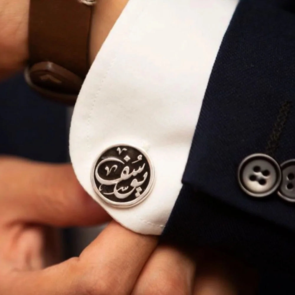 Close up of man adjusting dress shirt sleeve wearing circular silver cufflink with black Arabic calligraphic lettering