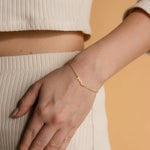 Woman wearing fine gold chain bracelet with june cursive script nameplate on wrist paired with cream ribbed outfit