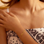 Close-up of a person wearing a gold bracelet with 'Stella' on it, against a neutral background.