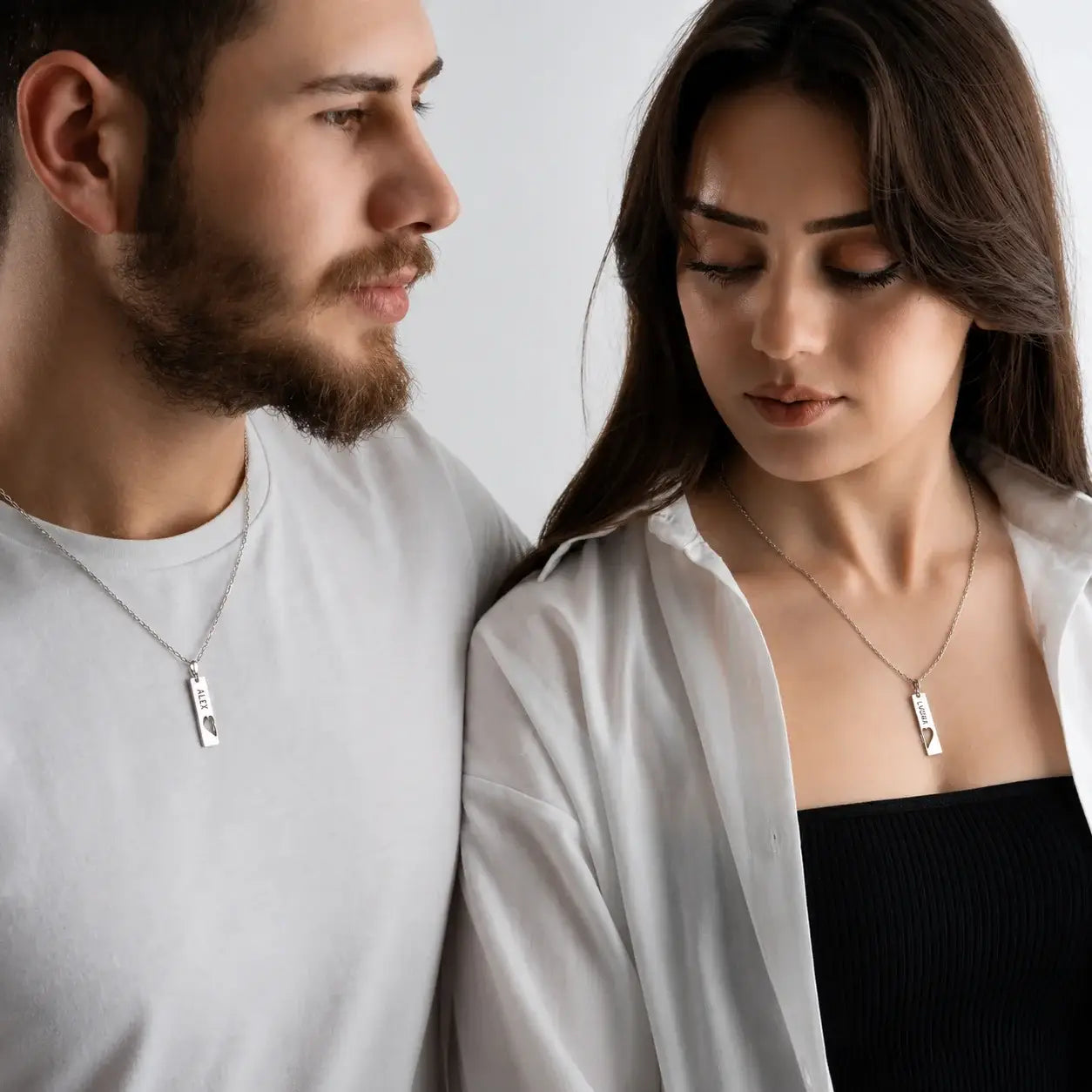 Man and woman wearing matching silver vertical tag necklaces with split heart engraved design
