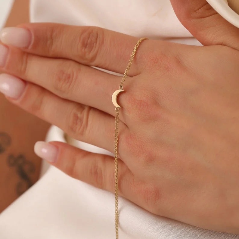 Close up of hand holding fine gold chain bracelet with small crescent moon pendant centered across fingers