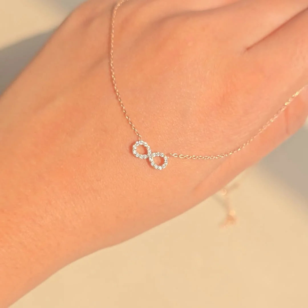 Hand wearing slim gold trace chain bracelet with pave clear crystal infinity symbol figure eight charm