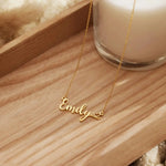 Gold chain necklace with Emily script nameplate and heart tail detail on wooden tray