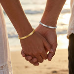 Couple holding hands while wearing personalized engraved cuff bracelets with custom message engraving, showcasing matching his and hers bangles.