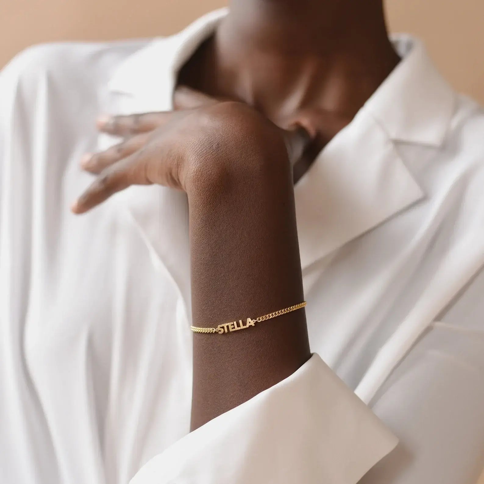 Gold bracelet with 'STELLA' on a person wearing a white shirt.