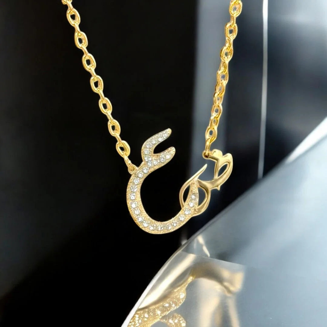Gold Arabic calligraphy letter necklace embellished with paved cubic zirconia rhinestones suspended on an oval link chain.
