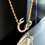 Gold Arabic calligraphy letter necklace embellished with paved cubic zirconia rhinestones suspended on an oval link chain.