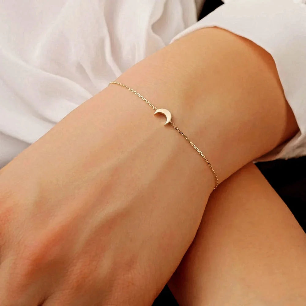 Woman wearing delicate gold chain bracelet with tiny crescent moon charm on wrist