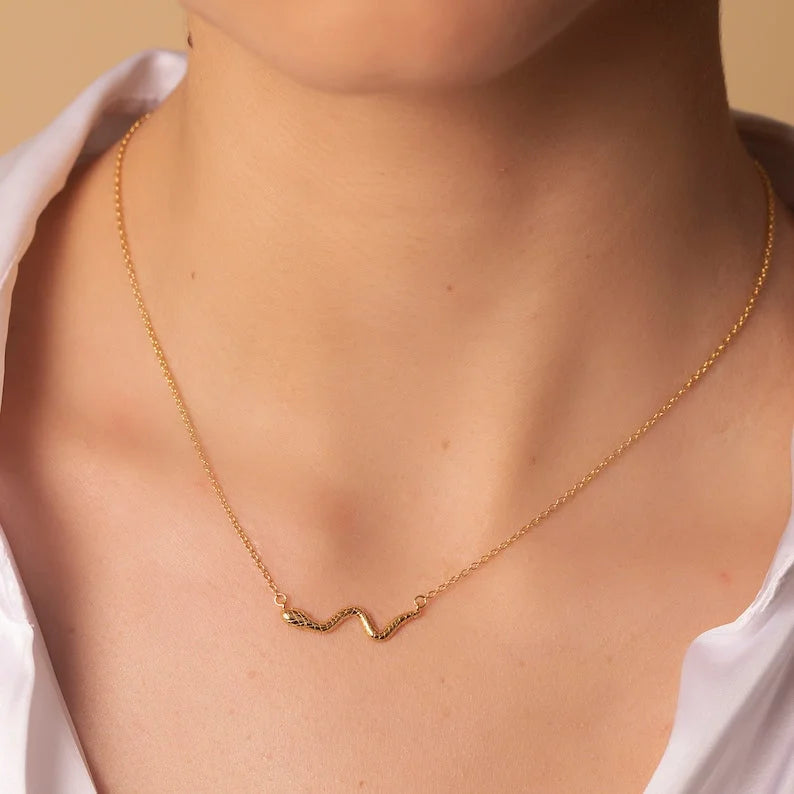 Woman wearing thin gold chain necklace with horizontal textured snake pendant