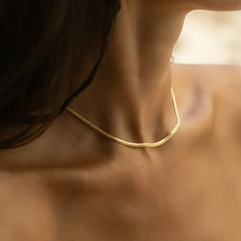 Woman wearing flat gold herringbone snake chain necklace resting around collarbone