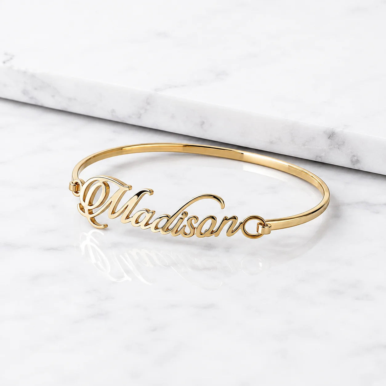 Madison gold name bangle bracelet with cursive personalized lettering on white marble background
