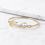 Madison gold name bangle bracelet with cursive personalized lettering on white marble background