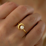 Close up of woman wearing gold open ring featuring white pearl paired with crescent moon design