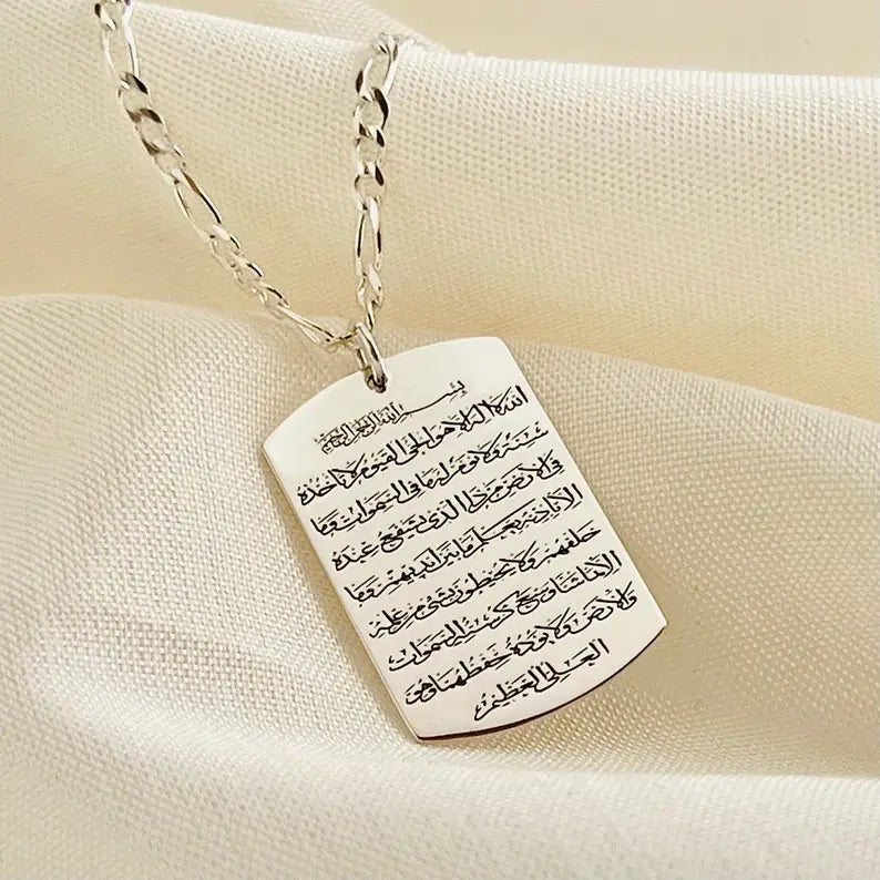 Men's sterling silver Ayatul Kursi necklace with engraved rectangular pendant displayed on a silver chain over a soft cream fabric background.