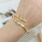 Gold bracelet with engraved names on a wrist, with a blurred background.