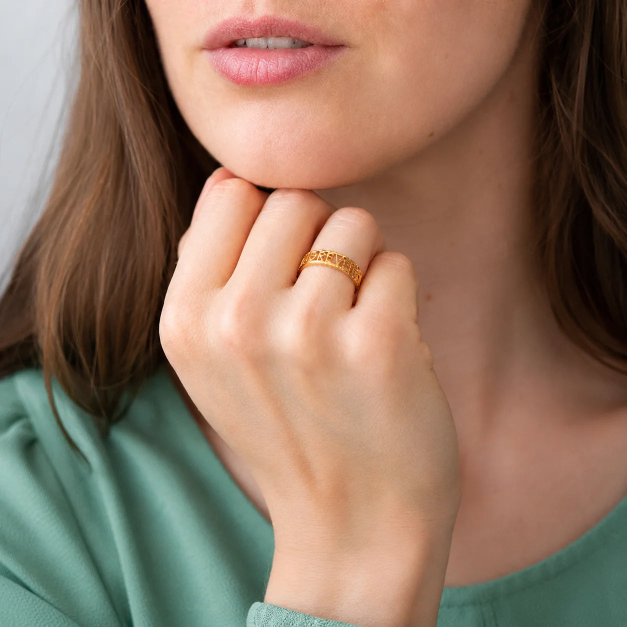 Woman with hand under chin wearing gold band ring featuring block letter cutout name design