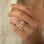 Woman wearing silver open band ring featuring round white pearl nestled next to crescent moon motif