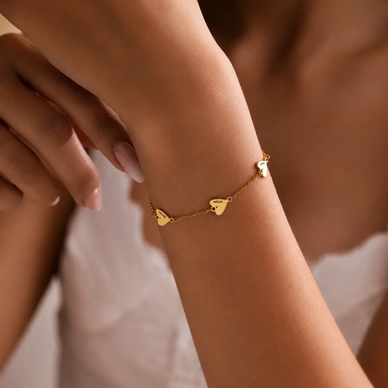 Personalized gold heart charm bracelet with engraved name charms worn on the wrist