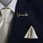 Personalized name coat pin with sleek script lettering attached to the lapel of a dark blue pinstripe suit jacket.
