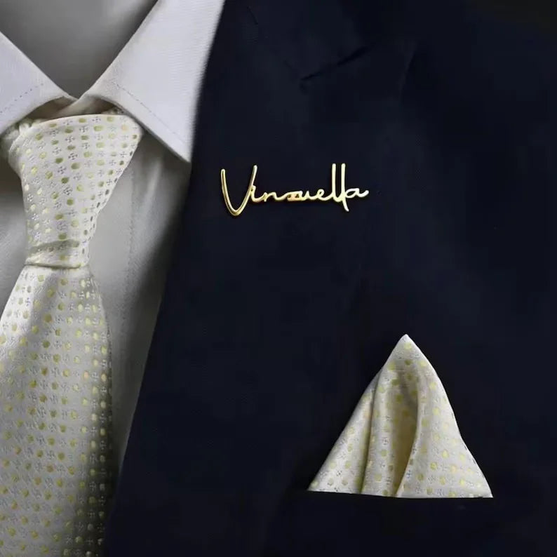 Personalized name coat pin with sleek script lettering attached to the lapel of a dark blue pinstripe suit jacket.