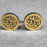 A pair of round gold-tone cufflinks with intricate cutout Arabic calligraphy patterns, set against a textured gray background.