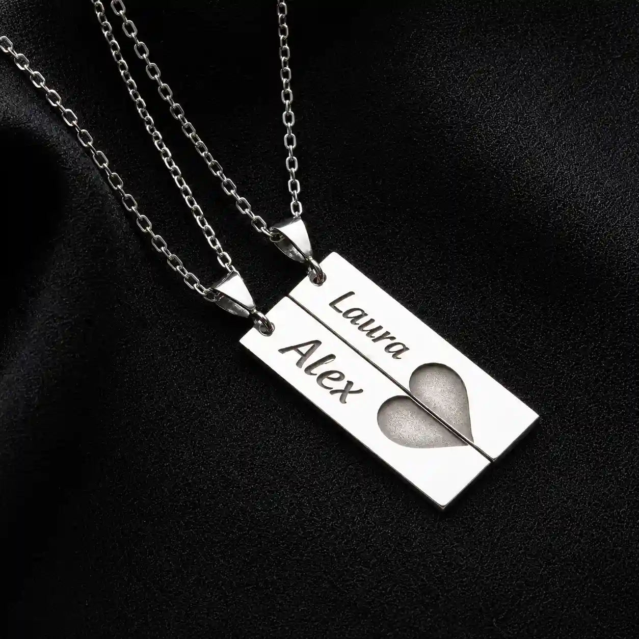 Silver rectangular split pendant necklaces engraved with Alex and Laura names forming a heart on black fabric
