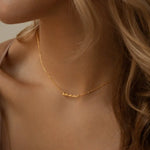 Woman wearing thin gold chain necklace with small anna cursive nameplate centered on neck