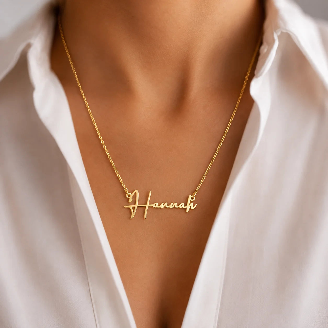 Woman wearing gold cable chain necklace with custom Hannah script nameplate against white blouse