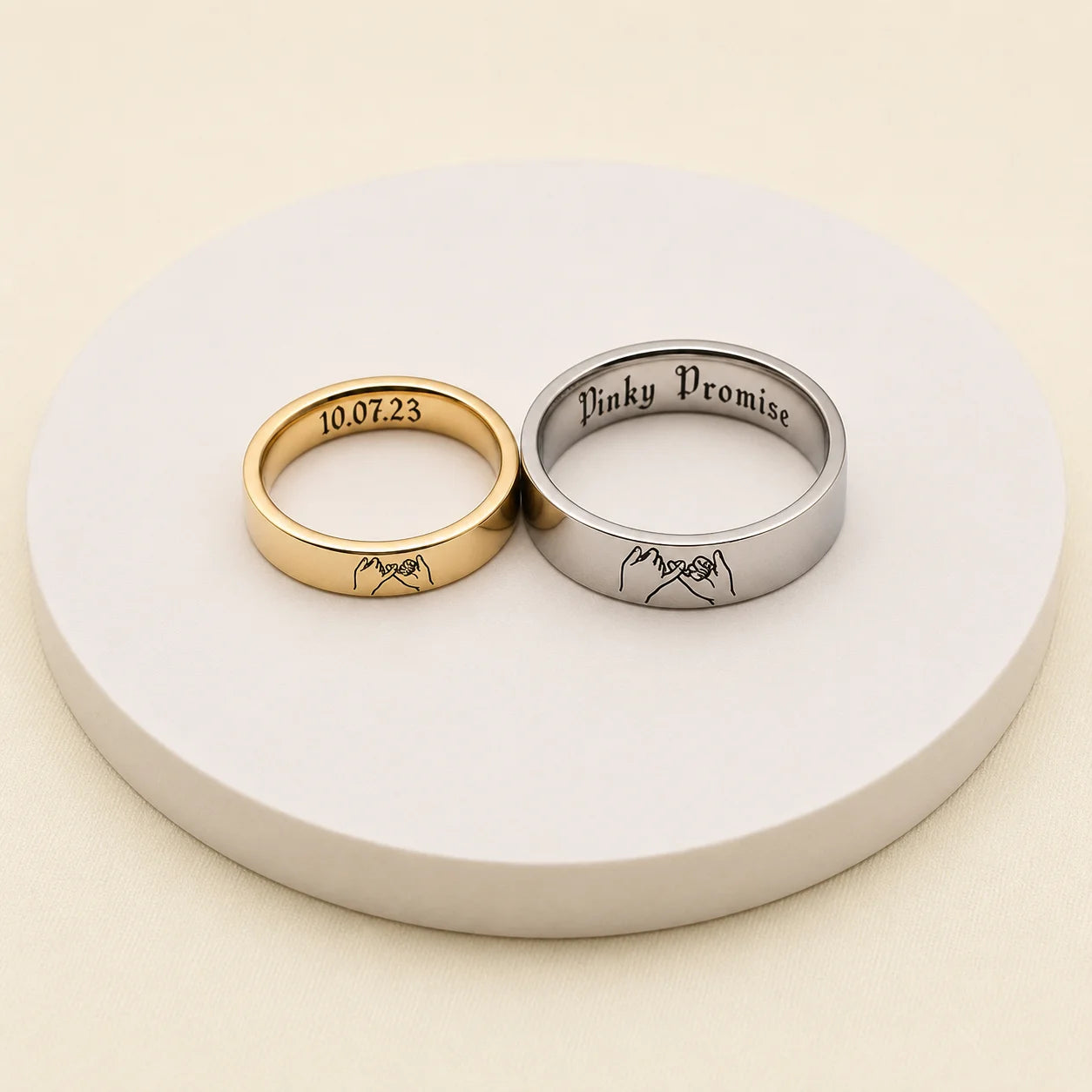 Gold and silver pinky promise rings with custom date and message engravings on a white display stand
