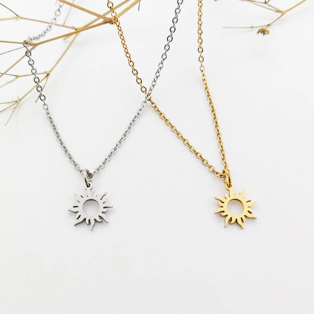 Two delicate chain necklaces with sun-shaped pendants, one in silver and one in gold, displayed on a white background with dried floral stems.