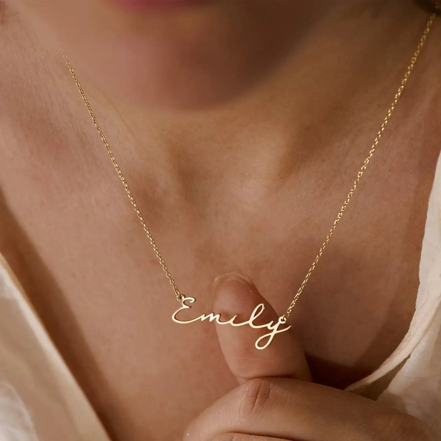 Close up of woman holding gold chain necklace with Emily cursive nameplate