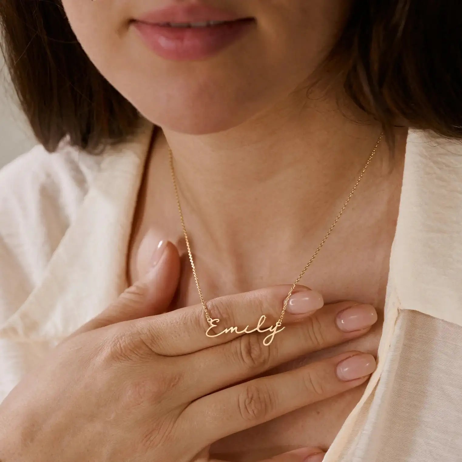 Woman holding gold chain necklace with delicate Emily script nameplate near neck