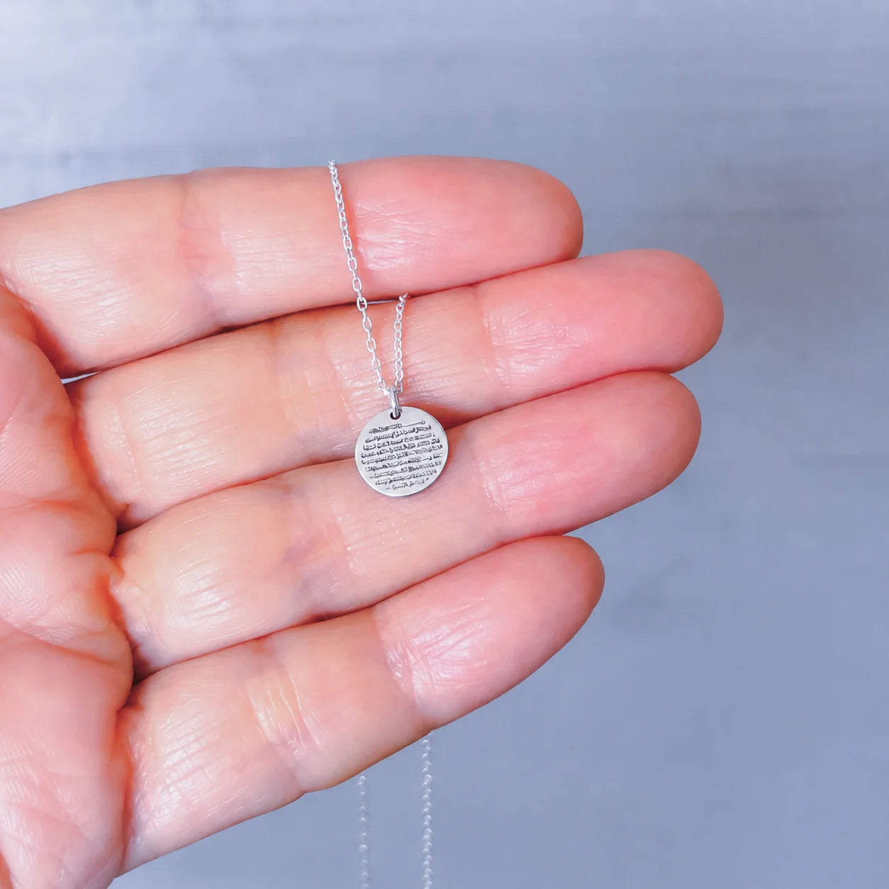 Close-up of a silver Ayat ul Kursi pendant necklace with detailed Arabic calligraphy, held by hand for elegant Islamic jewelry styling.