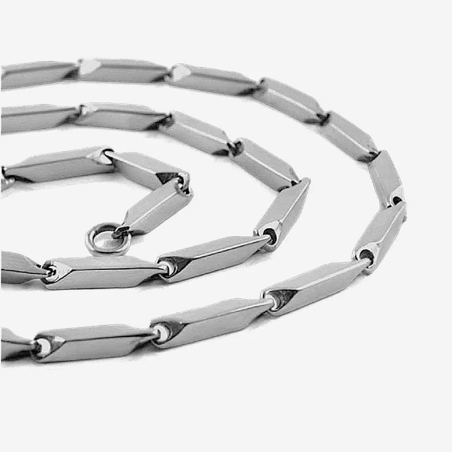 Close up of coiled silver necklace with connected cylindrical metal bar links on plain white background