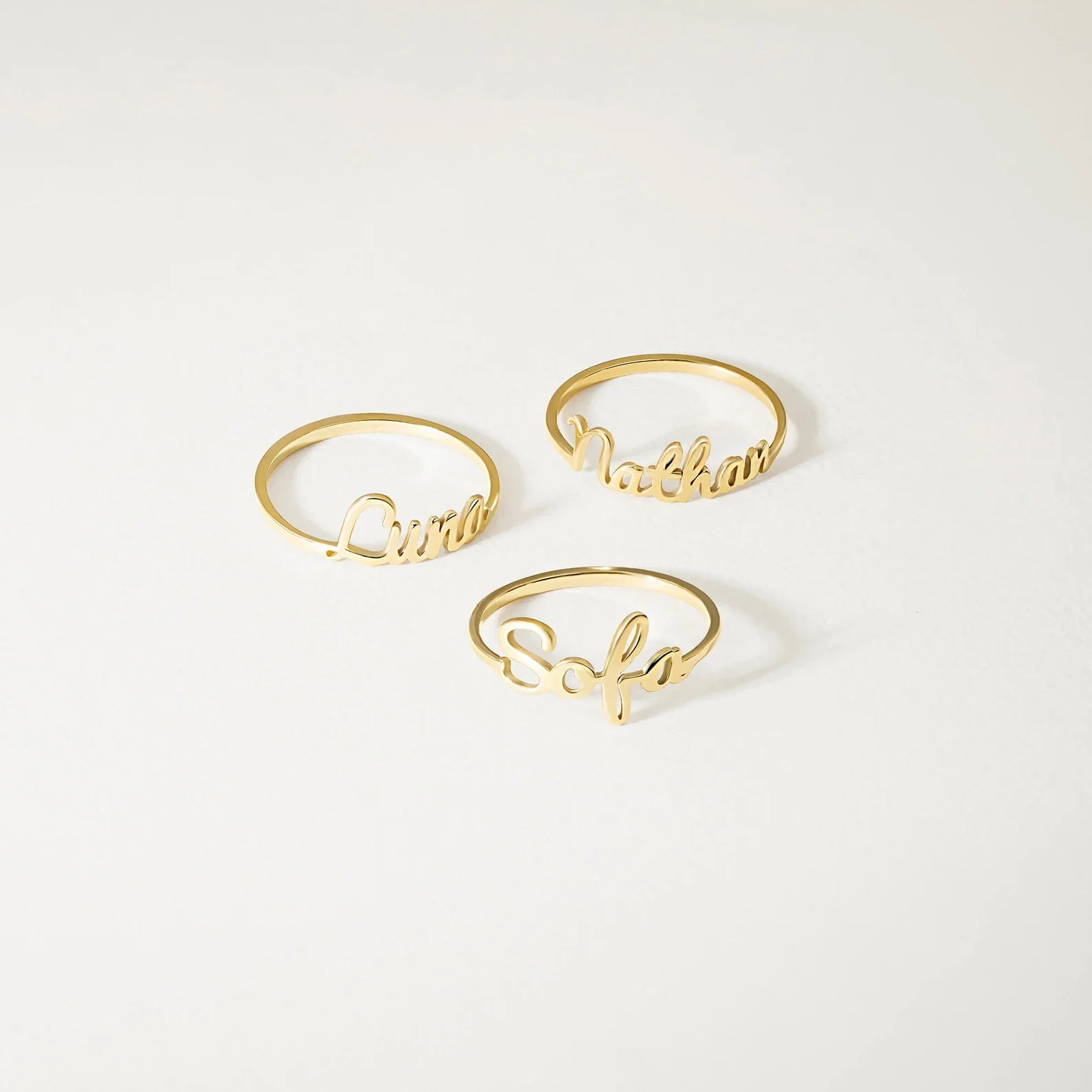 Three gold name rings spelling out 'Luna', 'Nathan', and 'Sofia' arranged on a clean white background.